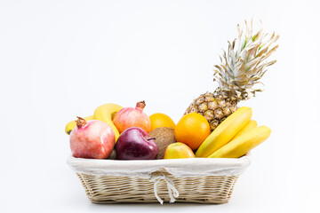 Fresh tropical fruits in the basket on a white backgraund. Balanced diet: pineapple, oranges, pomegranates, apples, bananas, coconuts