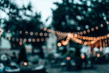 Fashion decoration string lights hanging in restaurant or cafe in the garden at summer party. Outdoor electric lamps. Blurred banner background