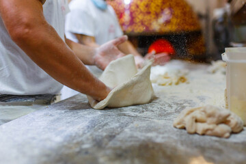 Pizzaiolo Napoletano mentre lavora l'impasto fatto a mano di una pizza napoletana sul banco di lavoro in marmo 
