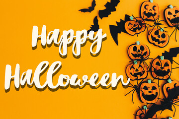 Happy Halloween text sign on pumpkins, jack o lanterns, spiders, bats border flat lay on orange background. Season's greeting card. Handwritten happy halloween text. Trick or treat