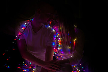 Couple in love sitting holding hands in Christmas lights. Silhouette.