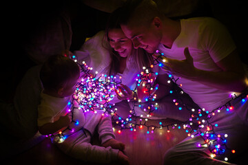 Mother, father and their little baby son sitting on a floor untangling fairy lights. Christmas concept.