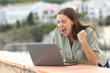 Excited woman watching media on laptop in a coast