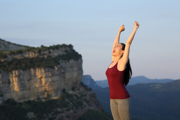 Happy runner raising arms in a mountain cliff