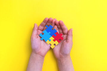World autism awareness day. The hands of a small child close up holding colorful puzzles on yellow...
