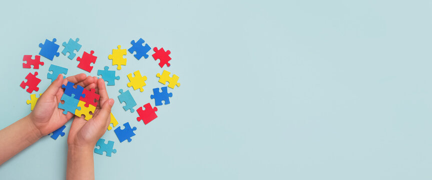 World autism awareness day. Autistic Pride Day. Hands of a small child holding colorful puzzles on blue background. Heart of puzzles.