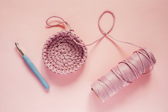 Crochet hook and pink color yarn on a pink background, knitting and crochet supplies, hobby and craft