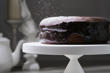 Tasty chocolate bundt  cake decorated icing sugar on the stand. Sieving powdered sugar on a...