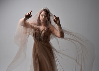 portrait of red haired  girl wearing a creamy fantasy gown and flowing veil fabric, like a fairy goddess costume.  standing  pose with elegant gestural hands, isolated on light studio background.