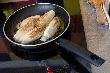 Cuisson des endives braisées dans une poêle sur une plaque de cuisson