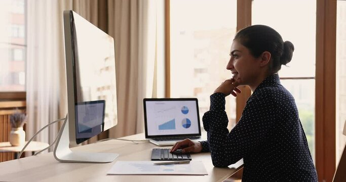 Happy young female professional financial analyst enjoy work on two powerful pc devices. Indian women freelancer use modern software on desktop and laptop computers to process statistic information