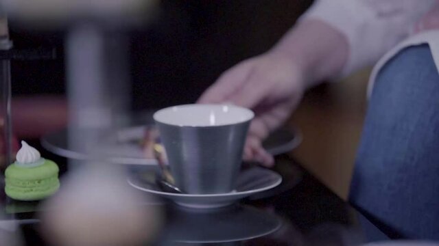 female holding silver tea cup setting on a small table with green macrons