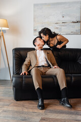 Obraz premium brunette woman in slip dress pulling tie while seducing man on couch