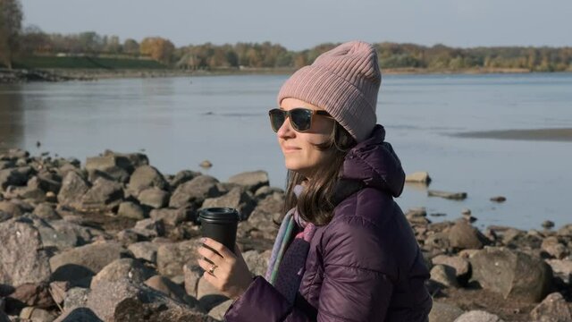 Young Hipster Woman in Sunglasses and Purple Coat Enjoying Sunny Autumn Day at the Stone Beach. Slow Motion. Harmony with Nature and People Concept