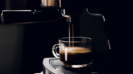 Hot coffee flow to a glass cup from espresso machine with nature light in the morning, Dark cinema tone and selective focus.