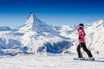 female skier resting on top of the mountain observing nature at ski resort on a beautiful sunny winter day. Matterhorn. Swiss Alps