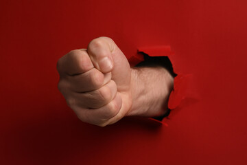 Man breaking through red paper with fist, closeup