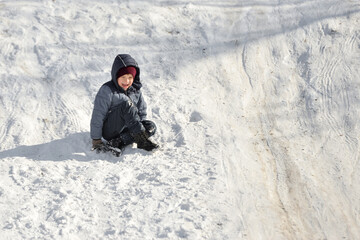 The boy goes down on his feet on a snowy hill in winter.