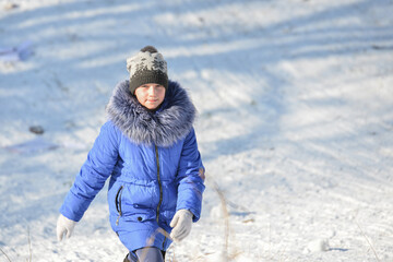 Fototapeta na wymiar A girl in a blue jacket is climbing a snowy hill.