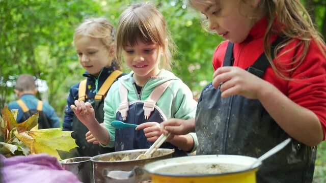 forest kindergarten Happy Preschool or school group children play Cook in swamp improvised kitchen. Outdoors small child have fun playing. Summer Camp, kid leisure educational entertainment in nature