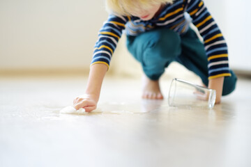Little boy wipes water spilled from a glass on the floor. Teaching a child to clean up after...