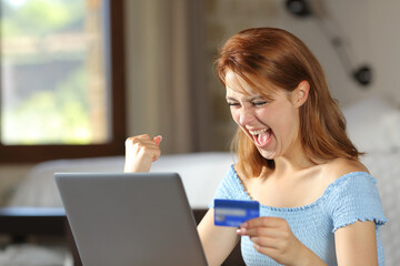 Fototapeta premium Excited woman buying online with credit card celebrating