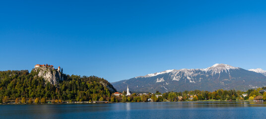 view of Lake Bled with the Bled Castle and village in autumn and snow-covered Julian Alps in the background