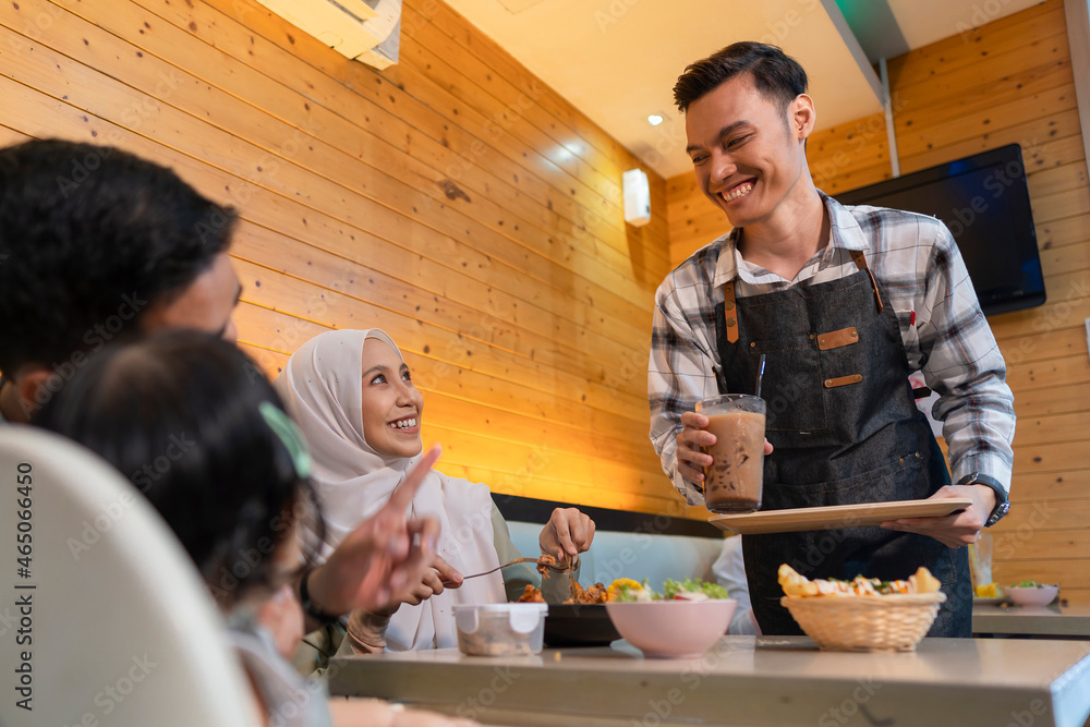 Wall mural young malay waiter at the restaurant serving food and smiling