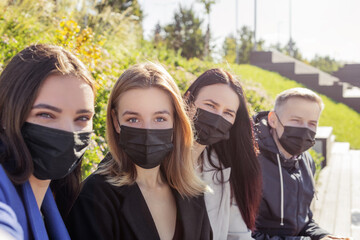 Group of young and attractive friends taking selfie with black medicine faces masks during coronavirus outbreak. Bright vivid backlight filter. Second from left woman is in camera focus