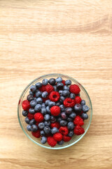 Glass bowl filled with raspberries and blueberries on wooden table. Top view.