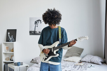 Waist up portrait of smiling African-American teenager playing electric guitar at home, copy space