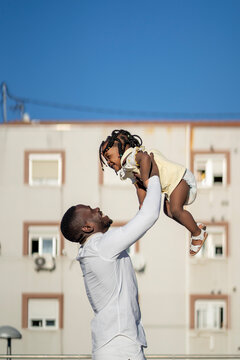 Happy black man playing with daughter on street in sunlight