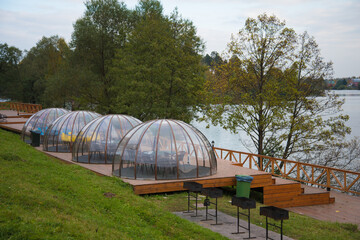 Transparent igloo-shaped hemispheres. Transparent gazebos stand on the river embankment. Division of companies during a pandemic