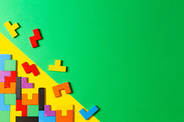 Different colorful shapes wooden puzzle blocks on green and yellow background. Geometric shapes in different colors, top view
