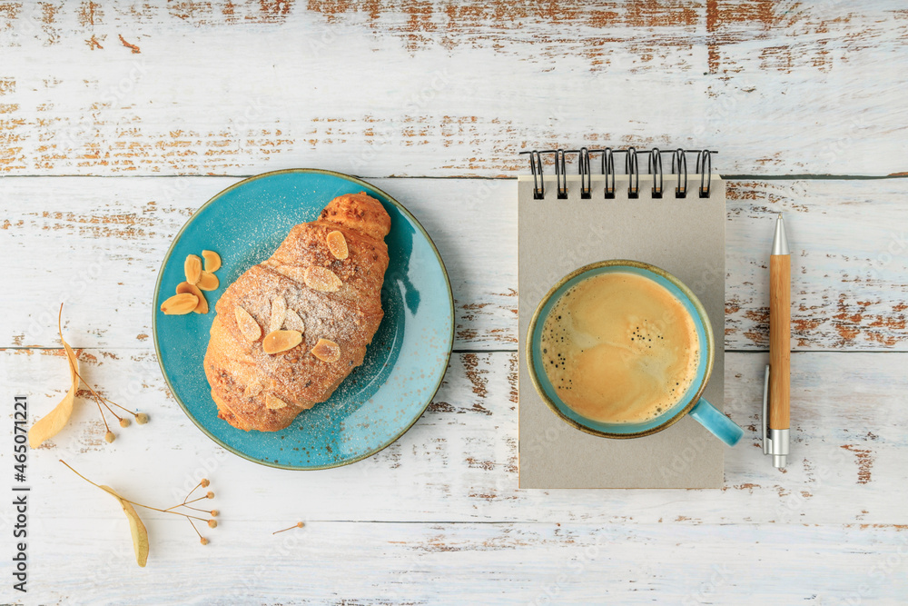 Wall mural Fresh baked almond nuts breakfast croissant on vintage turquoise plate and hot coffee cup