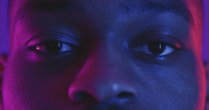 Close up shot of african american man opening eyes and looking seriously straight to camera, neon lights