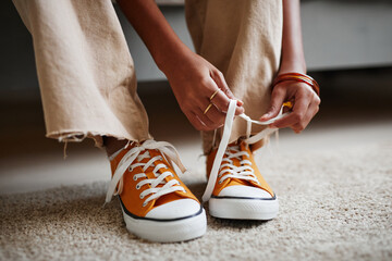 Close up of unrecognizable teenage girl tying laces on bright orange sneakers, copy space - obrazy, fototapety, plakaty