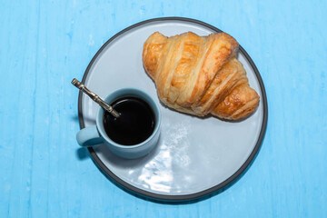 Breakfast food croissant in plate and coffee on blue table.