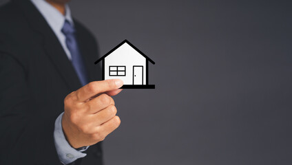 Fototapeta na wymiar Business and real estate concept. A businessman's holding a mini paper house while standing over gray background. Space for text. Close-up photo. Property insurance and security