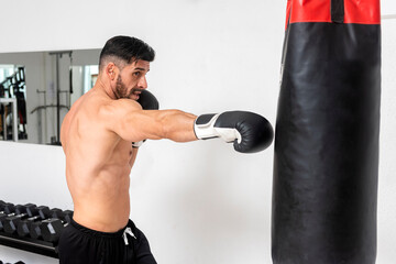 muscular young man, bare-chested, wearing boxing gloves training in gym