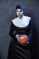 Beautiful woman wearing nun costume and halloween makeup over dark gray background	