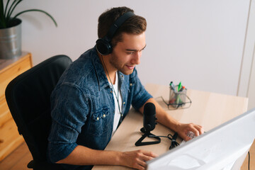 High-angle view of positive audio blogger streamer male wearing headphones sitting at desk with...
