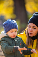 boy in autumn leaves looking with mom at ladybug