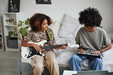 Portrait of two African-American teenagers playing electric guitars at home and smiling happily,...