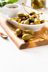 Pickled capers close up. Preserved fruits capers in a white plate on a light background.