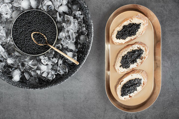 Black caviar in can on ice and bread with butter on golden plate