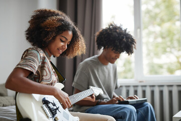 Side view portrait of two African-American teenagers playing electric guitars at home and smiling...