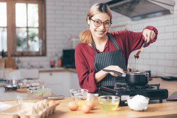 Beautiful young woman  is mixing batter, looking at camera and smiling while baking in kitchen at home ,decorating a cake of chocolate cake,cooking class, culinary, bakery, food and people concept