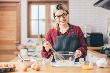 Beautiful young woman  is mixing batter, looking at camera and smiling while baking in kitchen at home ,decorating a cake of chocolate cake,cooking class, culinary, bakery, food and people concept