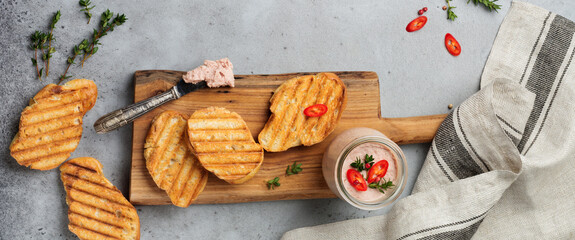 Chicken homemade pate from liver with red pepper, thyme twigs and toasted bread slices on wooden old board on gray concrete or stone background. Selective focus. Top view. Copy space